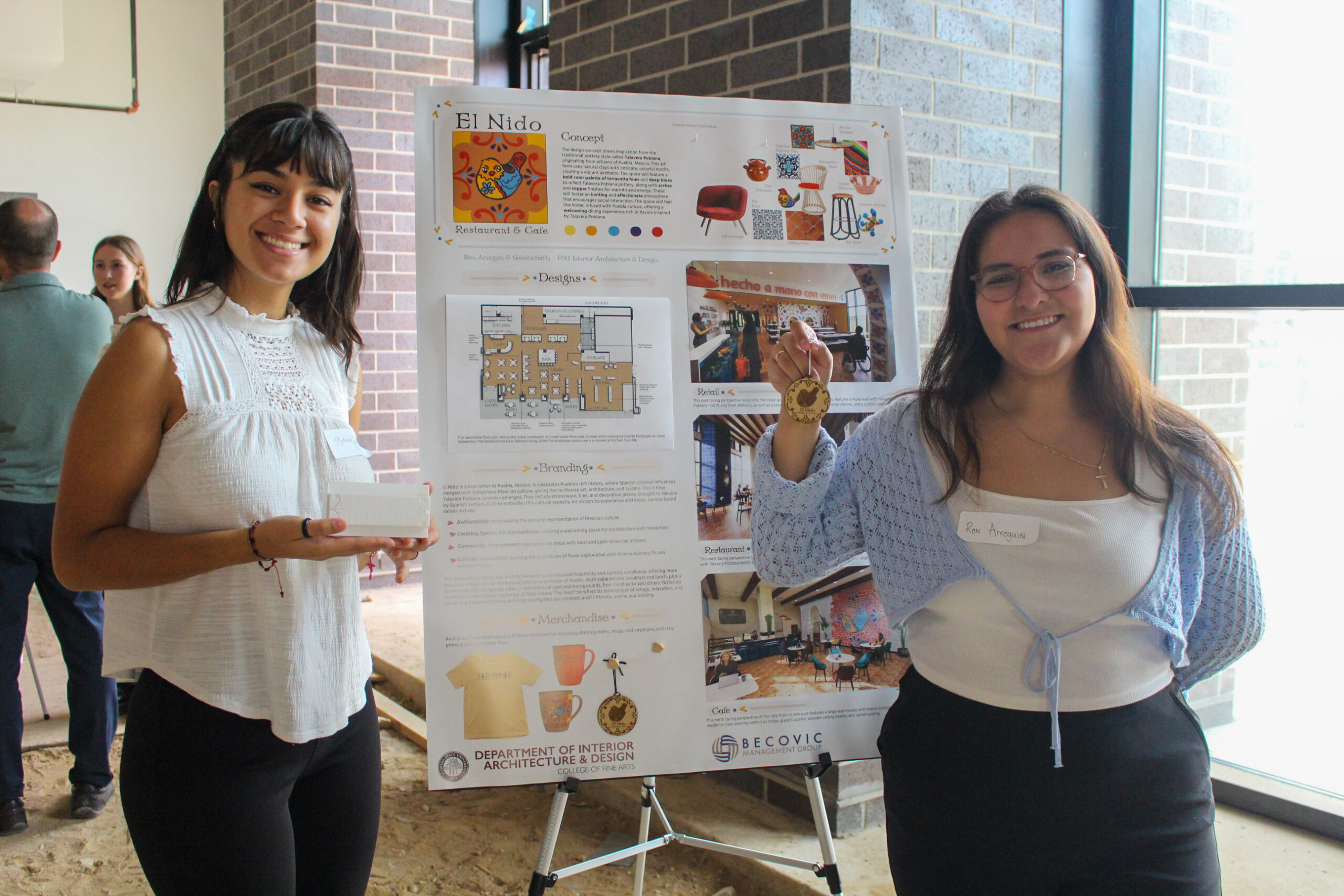 Two professional young women post in front of a posterboard in a sunny room,