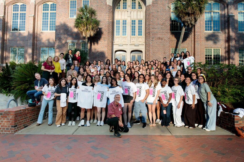 A group of students and professors posing with Tee shirts in front of a brick building